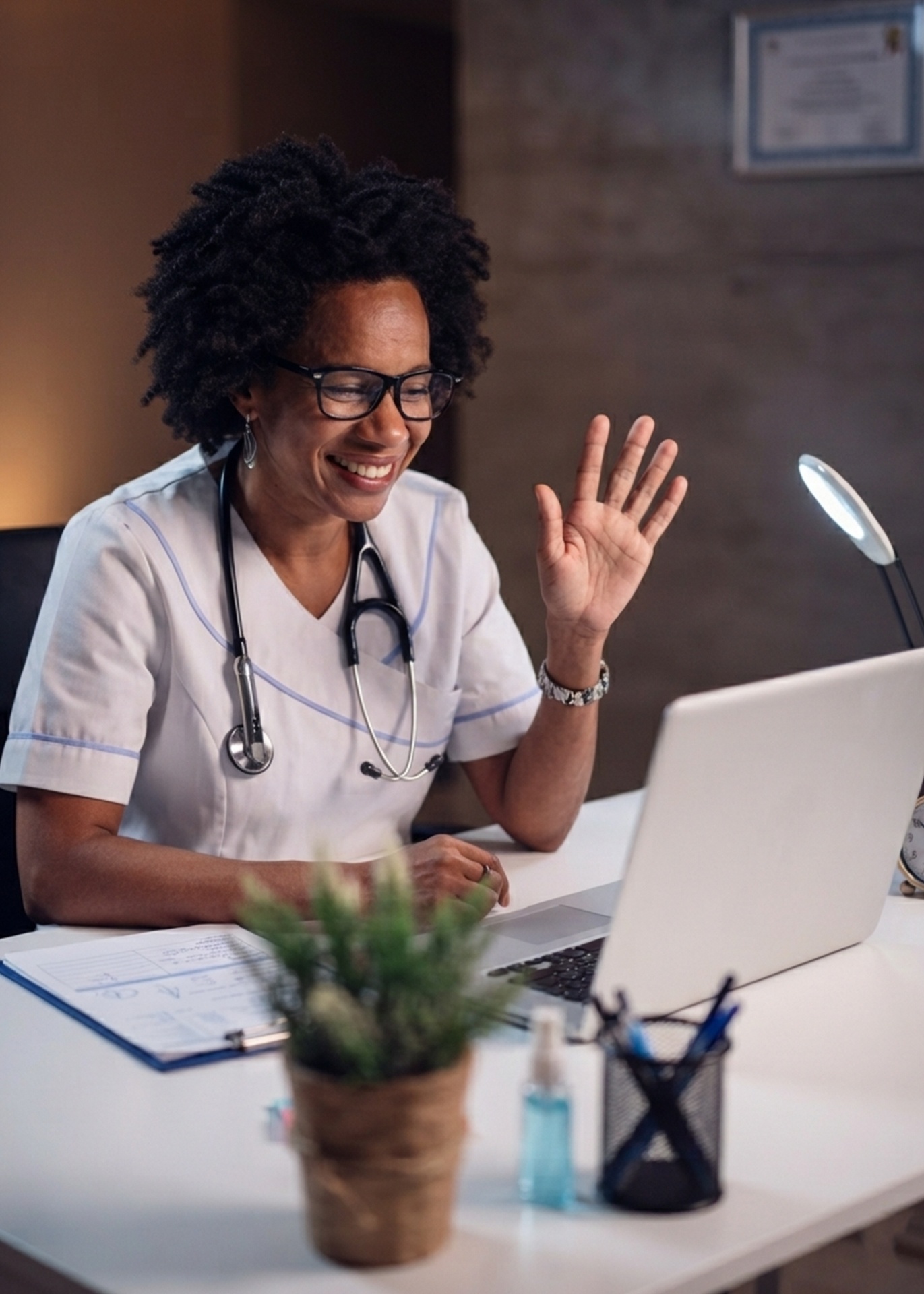 African nurse smiling and waving during a video call with a patient